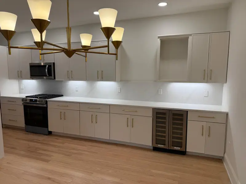 Painted white kitchen cabinets with long brass pulls, quartz backsplash and gold chandelier in Newton, MA