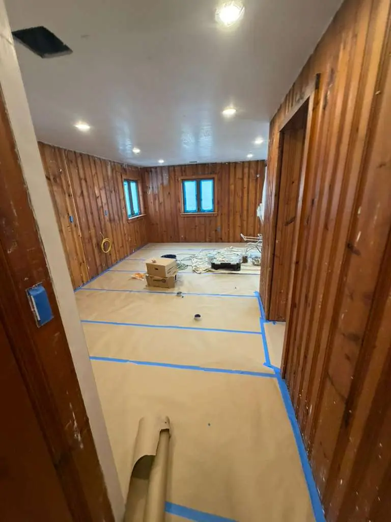 Pine-paneled room with protected floors and taped edges ready for painting
