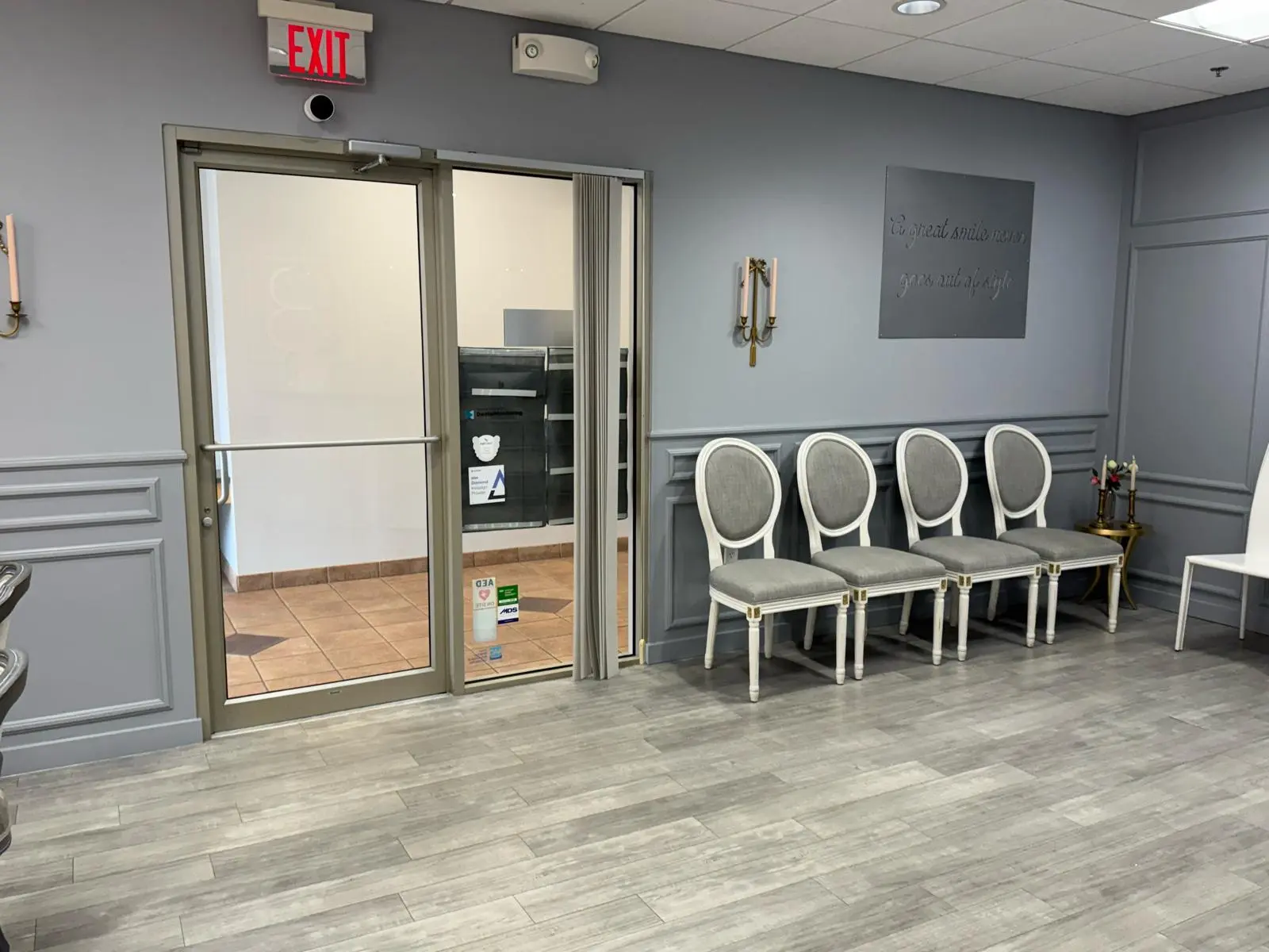 Dental office reception area with gray paneled walls, white chairs and glass entry door